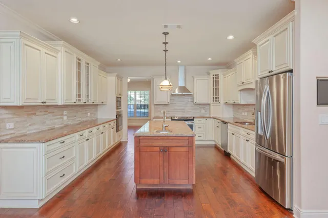 a large kitchen with stainless steel appliances granite countertop a stove a sink dishwasher a refrigerator and white cabinets with wooden floor