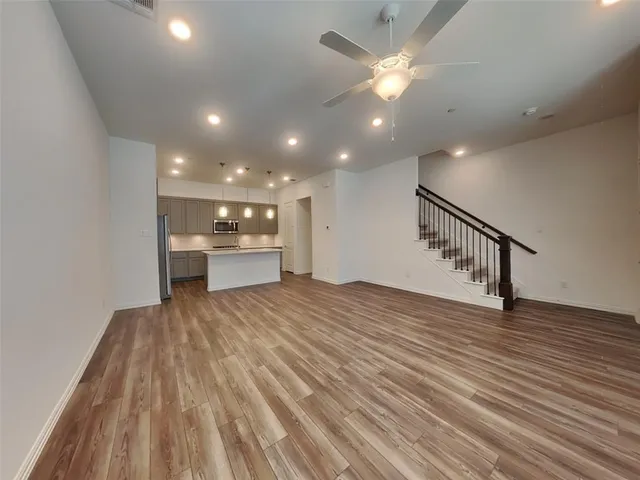 a view of an empty room with wooden floor and a ceiling fan