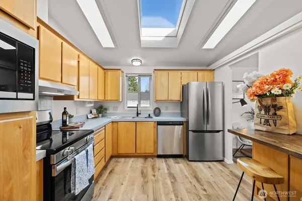 a kitchen with granite countertop a refrigerator a sink dishwasher a stove top oven a dining table and chairs with wooden floor