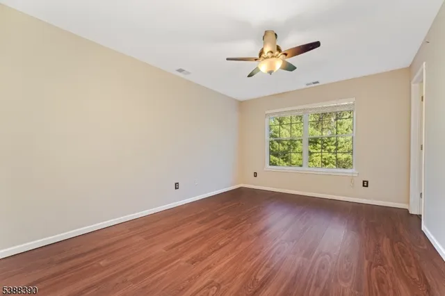 an empty room with wooden floor chandelier fan and windows