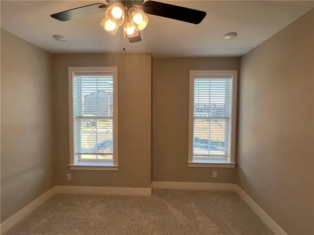 an empty room with chandelier fan and windows