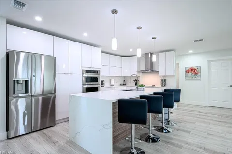 a large kitchen with stainless steel appliances kitchen island a stove a refrigerator a sink dishwasher a oven with white cabinets and wooden floor