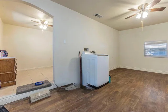a view of an empty room with wooden floor and a ceiling fan