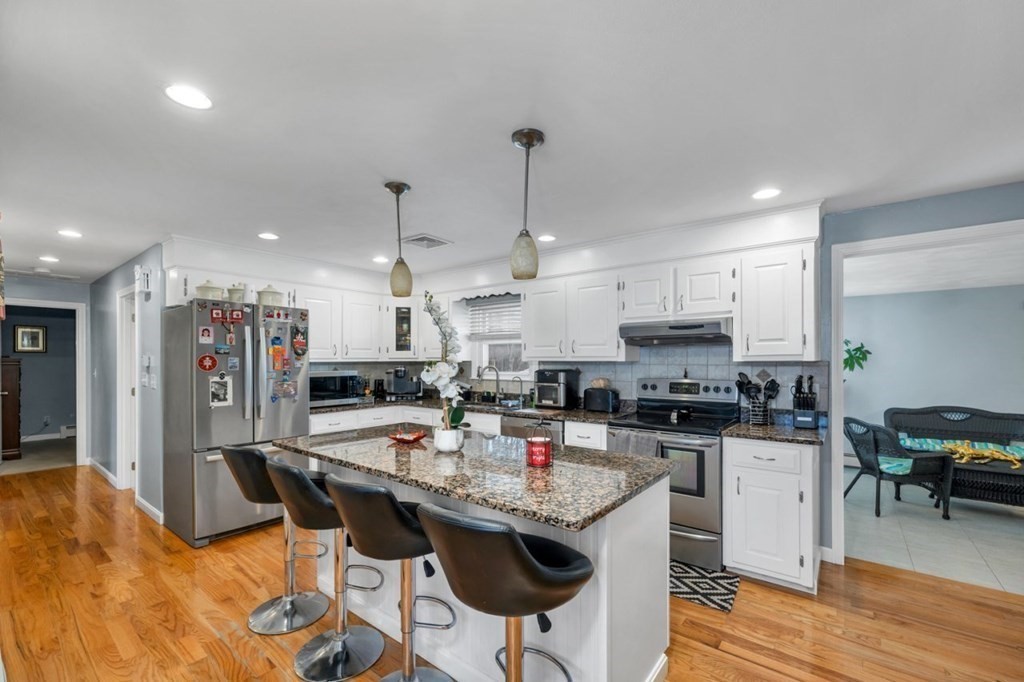 a kitchen with stainless steel appliances kitchen island granite countertop a dining table chairs stove refrigerator and cabinets