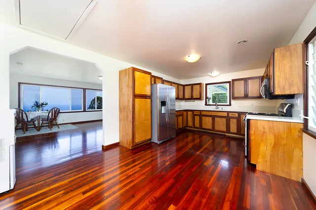 a living room with stainless steel appliances furniture wooden floor and a kitchen view