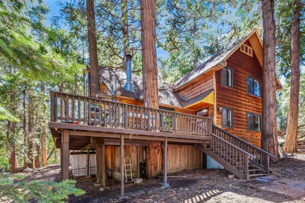 a view of a wooden house with large trees and wooden fence