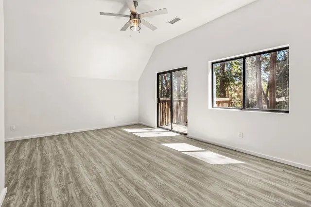an empty room with wooden floor chandelier fan and windows