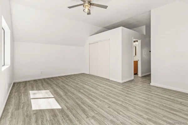 an empty room with wooden floor chandelier fan and windows