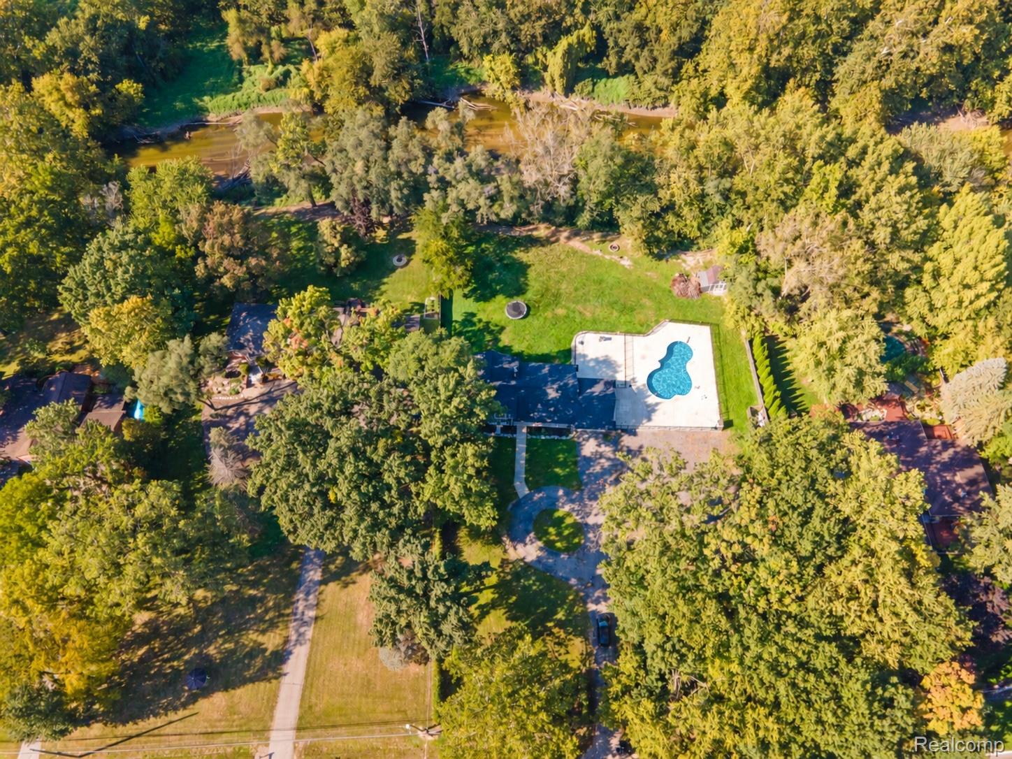 15879 Millar Road Clinton Township, MI 48036 - Photo 64 of 65 Expansive property featuring a winding river, lush surrounding trees, a freeform swimming pool with surrounding patio, and a manicured lawn