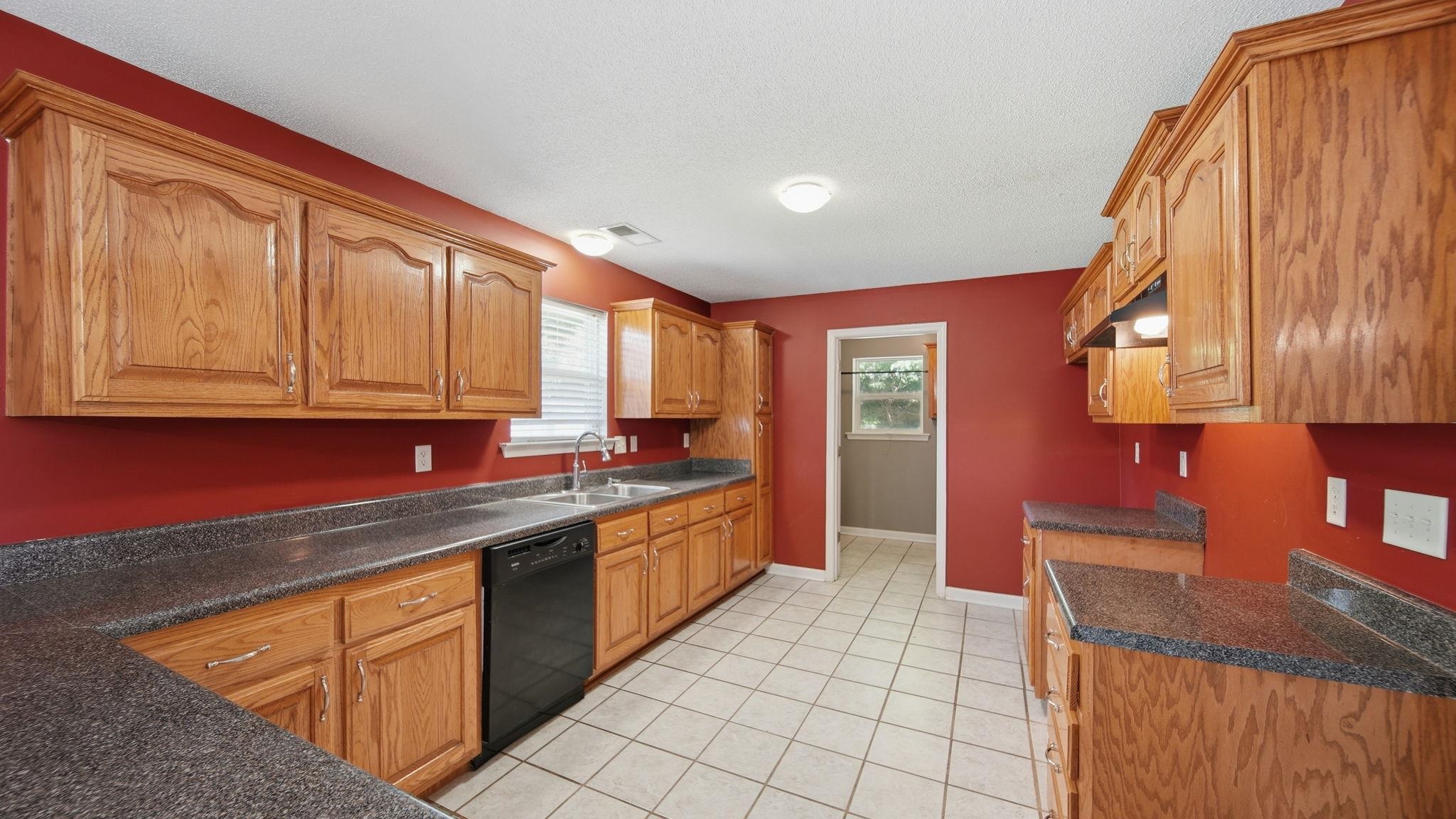 217 Rae Drive Munford, TN 38058 - Photo 11 of 40 Spacious kitchen featuring extensive wood cabinetry, dark speckled countertops, a double basin stainless steel sink, black built-in dishwasher, and white square tile flooring
