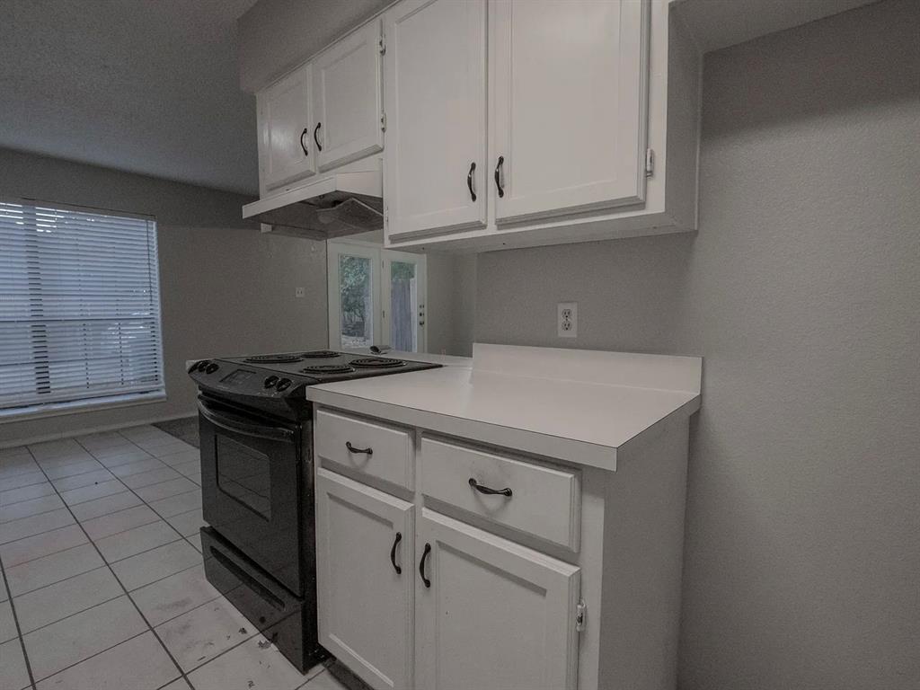 675 Harbor Drive North, Unit D Azle, TX 76020 - Photo 4 of 8 Kitchen featuring black range with electric cooktop, white cabinets, light countertops, under cabinet range hood, and light tile patterned floors