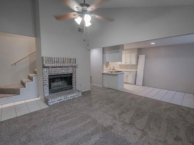 675 Harbor Drive North, Unit D Azle, TX 76020 - Photo 7 of 8 Unfurnished living room featuring light tile patterned floors, ceiling fan, a fireplace, light carpet, and vaulted ceiling