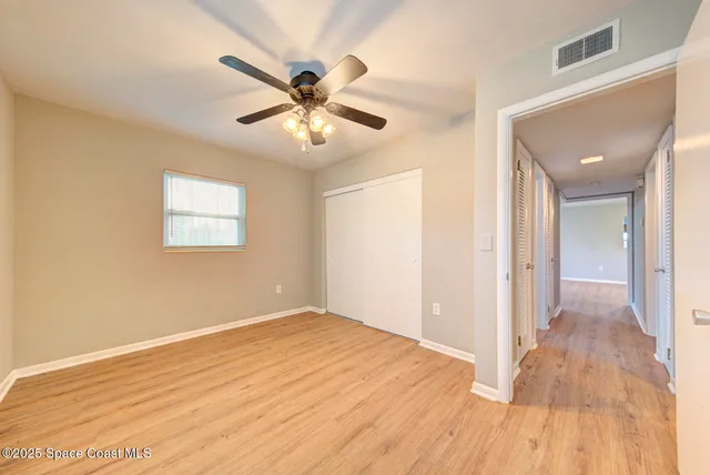 an empty room with wooden floor fan and windows