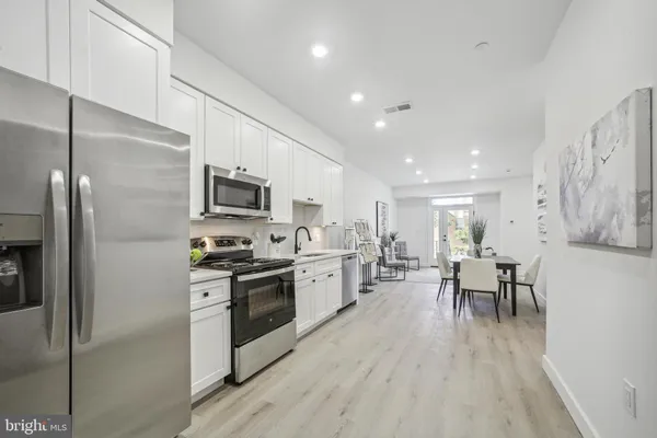 a kitchen with stainless steel appliances granite countertop a refrigerator a stove top oven a sink dishwasher a dining table and chairs with wooden floor