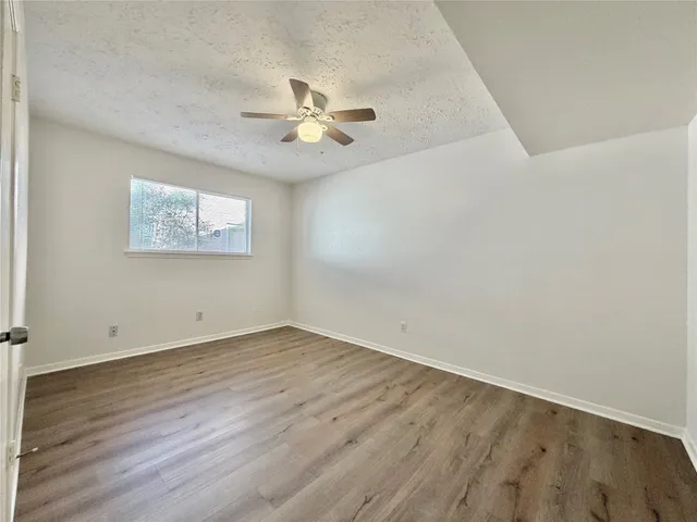 an empty room with wooden floor fan and windows