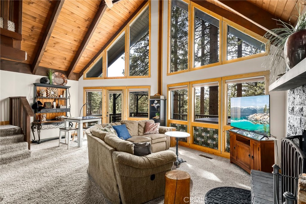 View of living area features dining area or game table, full floor to ceiling windows with view of trees/woods.  Deck is wrap around to BBQ area, has sitting area and sauna and overhead trellis that can be covered.