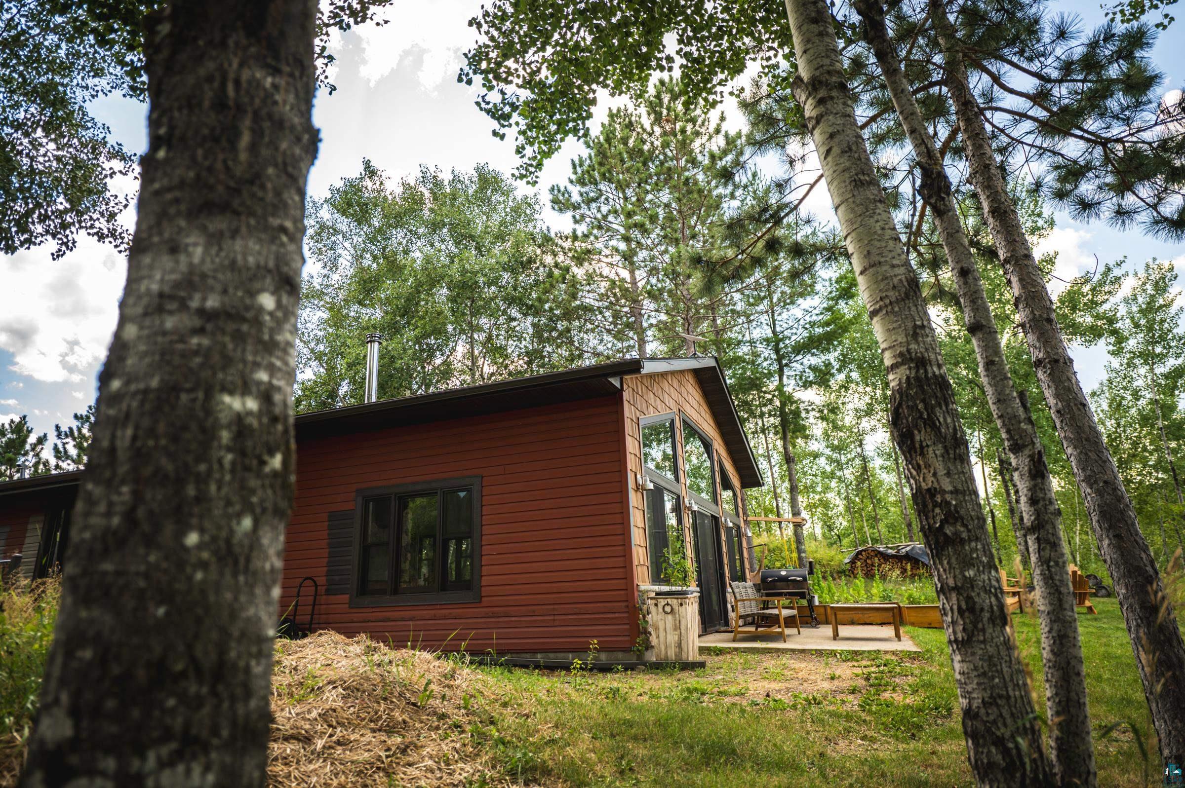 14635 Canadian Border Road Ely, MN 55731 - Photo 44 of 94 Red-sided property featuring a concrete patio, large picture windows, a chimney, and surrounding mature trees