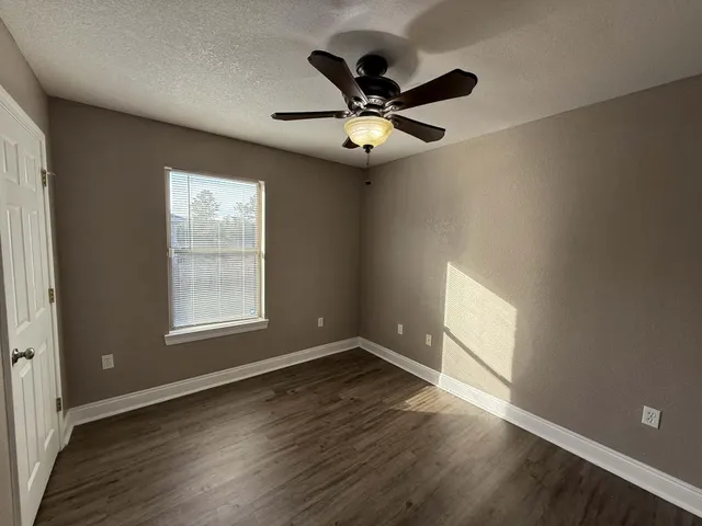an empty room with wooden floor fan and windows