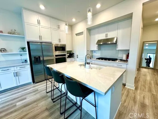 a kitchen with stainless steel appliances a stove a sink a microwave a refrigerator and white cabinets with wooden floor