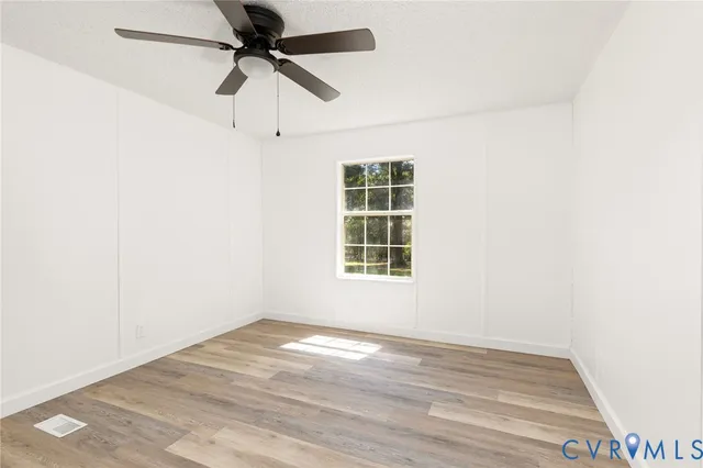 an empty room with wooden floor ceiling fan and windows