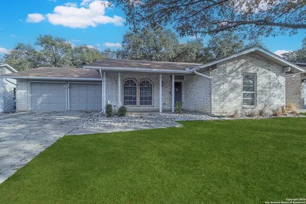 a view of a house with brick walls and a yard with trees
