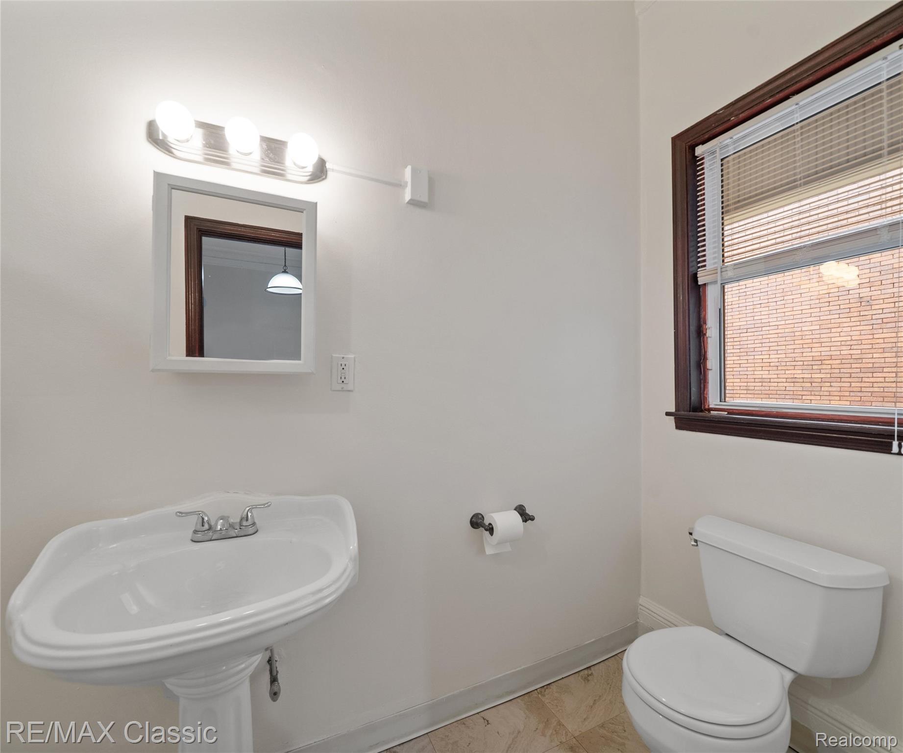 3941 Trumbull Detroit, MI 48208 - Photo 8 of 46 Pedestal sink with chrome faucet, wall-mounted mirror, and vanity lighting