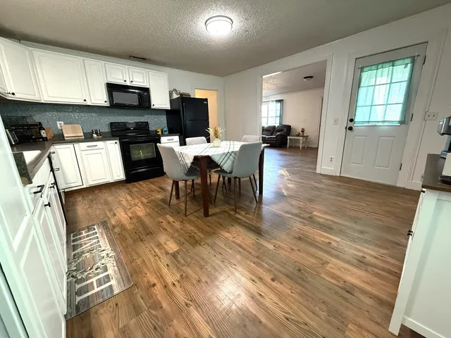 a living room with stainless steel appliances furniture a fireplace a flat screen tv and a kitchen view