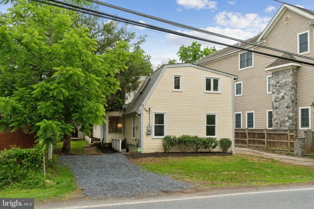 a view of a white house next to a yard with big trees