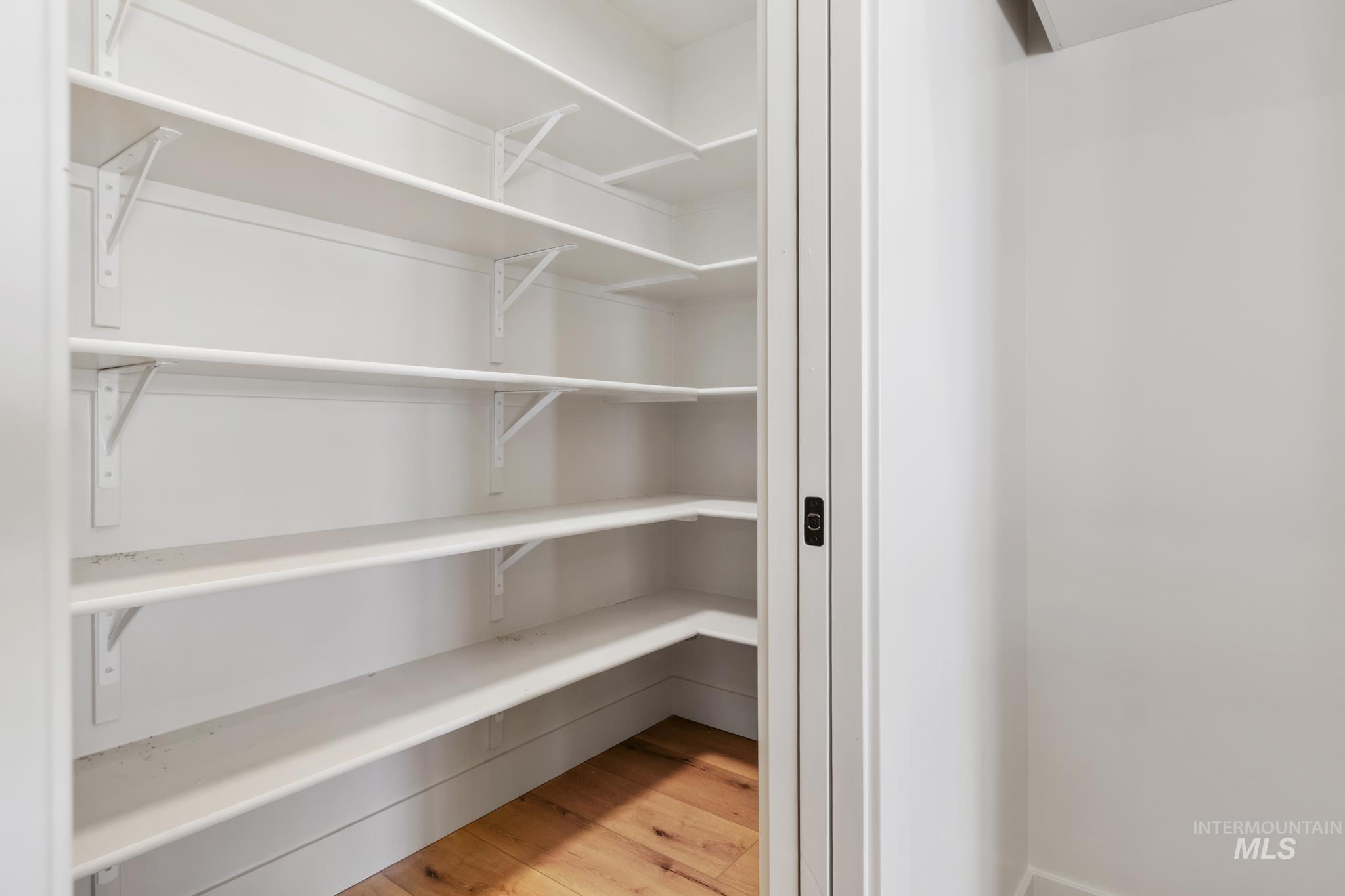 321 North 11th Street Parma, ID 83660 - Photo 18 of 36 Walk-in pantry featuring light wood-finish flooring, white shelving, white walls, and a contemporary black door handle