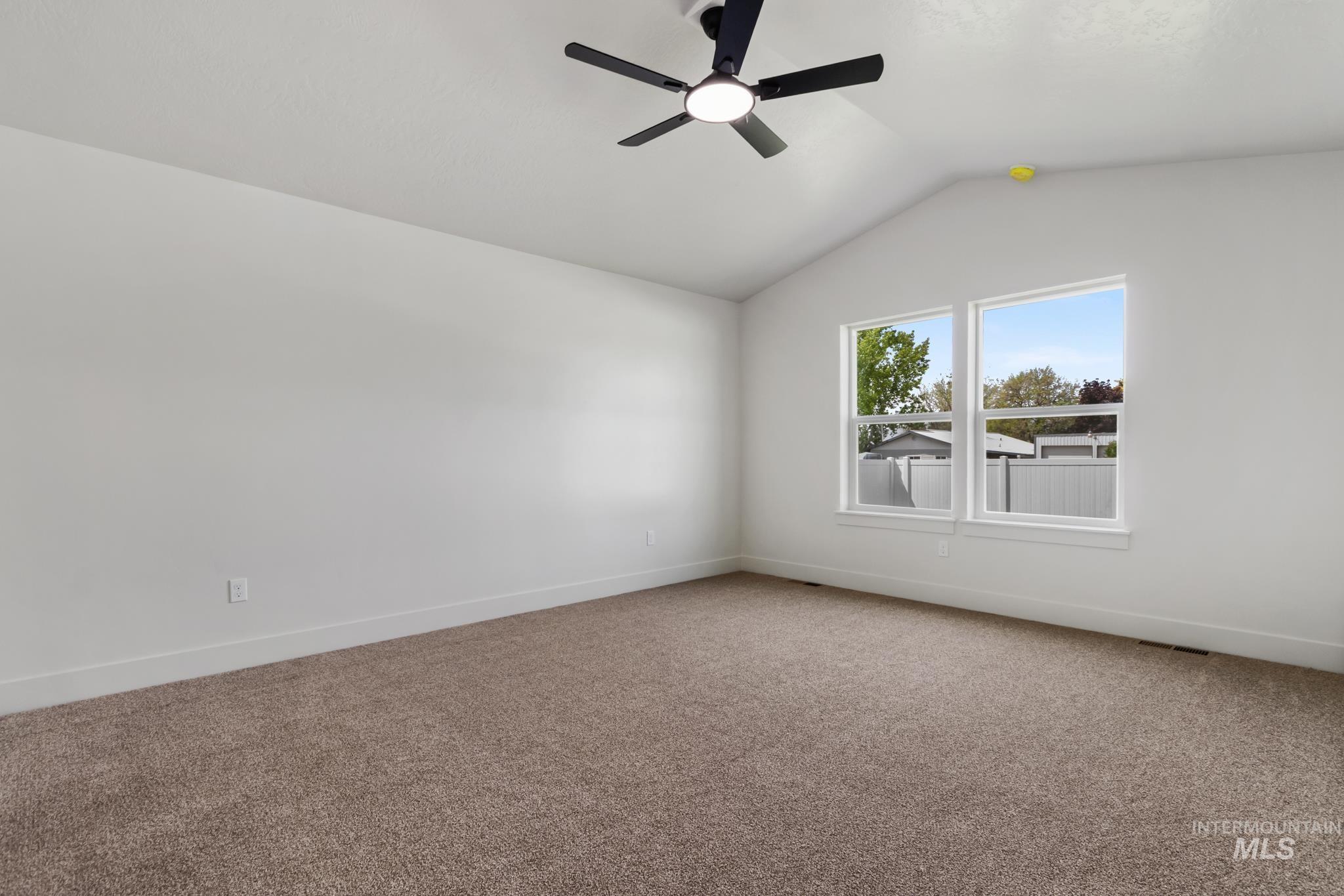321 North 11th Street Parma, ID 83660 - Photo 24 of 36 Spacious room featuring vaulted ceilings, a ceiling fan with integrated lighting, two large windows, plush carpeting, and white baseboards