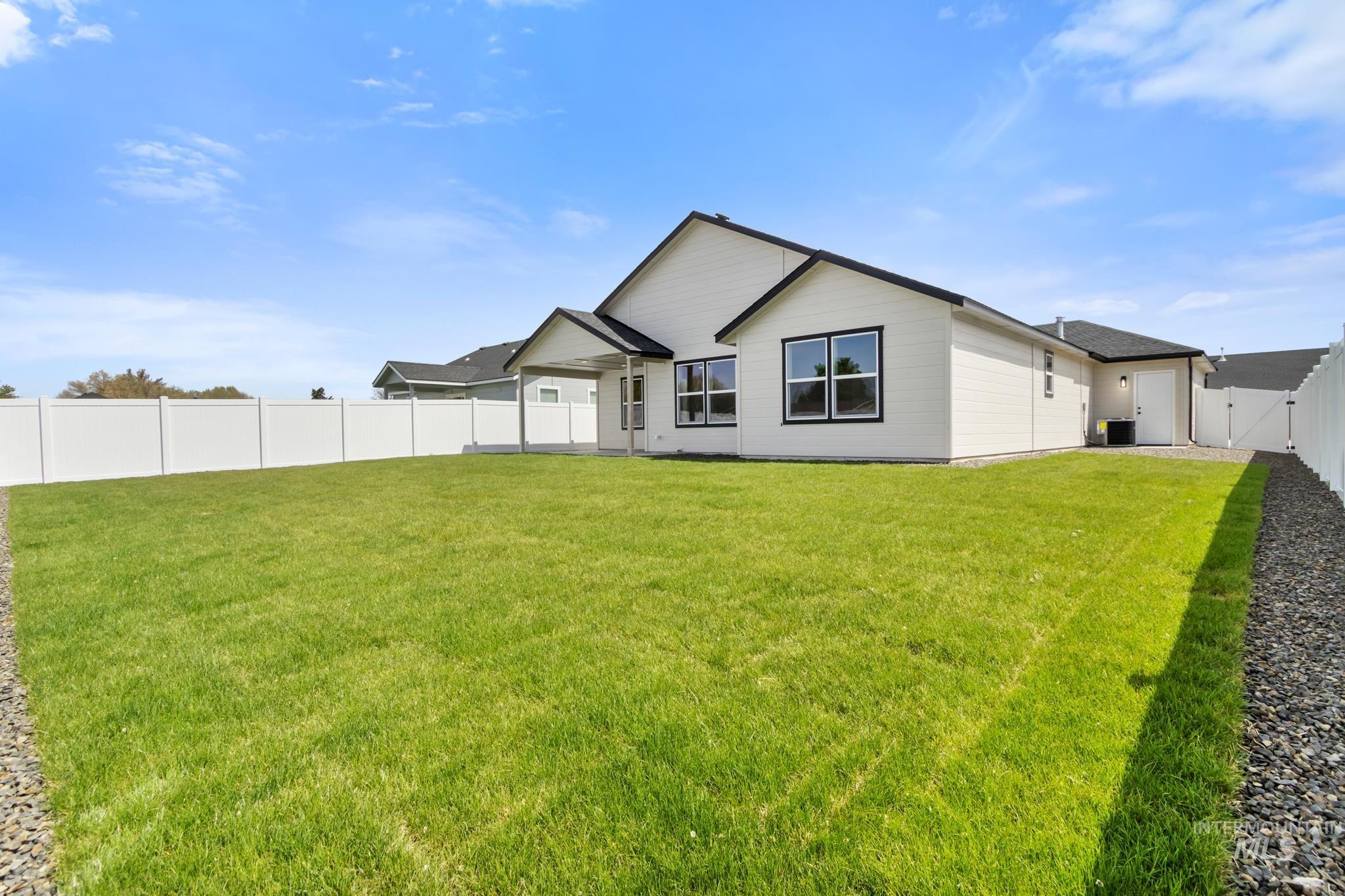 321 North 11th Street Parma, ID 83660 - Photo 34 of 36 Expansive backyard featuring a manicured lawn, a full white vinyl fence, a covered patio, and a gravel-lined side yard