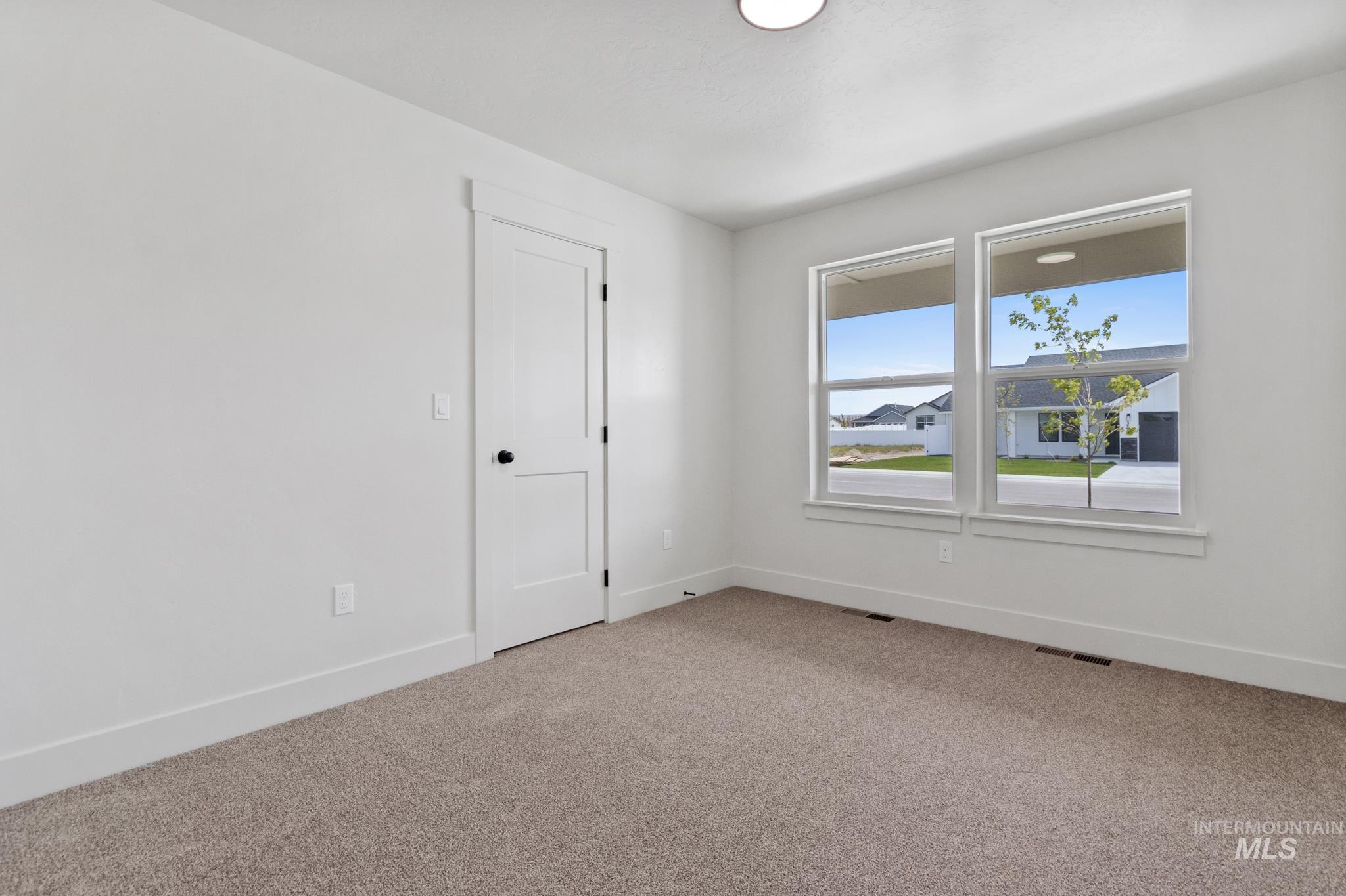 321 North 11th Street Parma, ID 83660 - Photo 4 of 36 Bright interior space featuring two large windows, neutral carpet flooring, white walls, a white two-panel door with black hardware, and recessed ceiling lighting