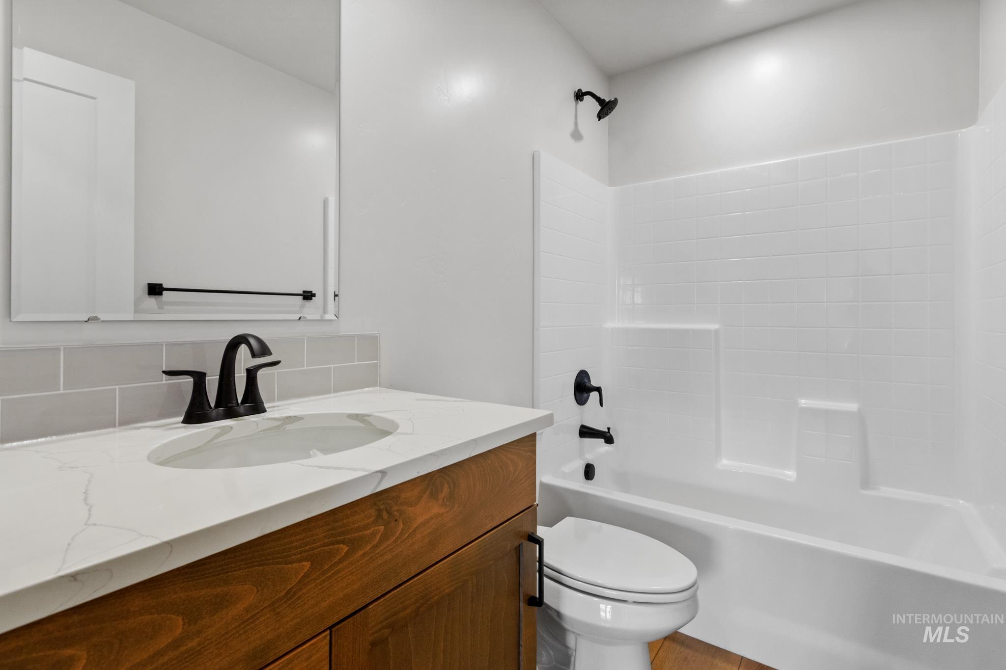 321 North 11th Street Parma, ID 83660 - Photo 6 of 36 Bathroom featuring a wood-finish vanity with a white countertop and oval undermount sink, matte black faucet, and a white subway tile backsplash