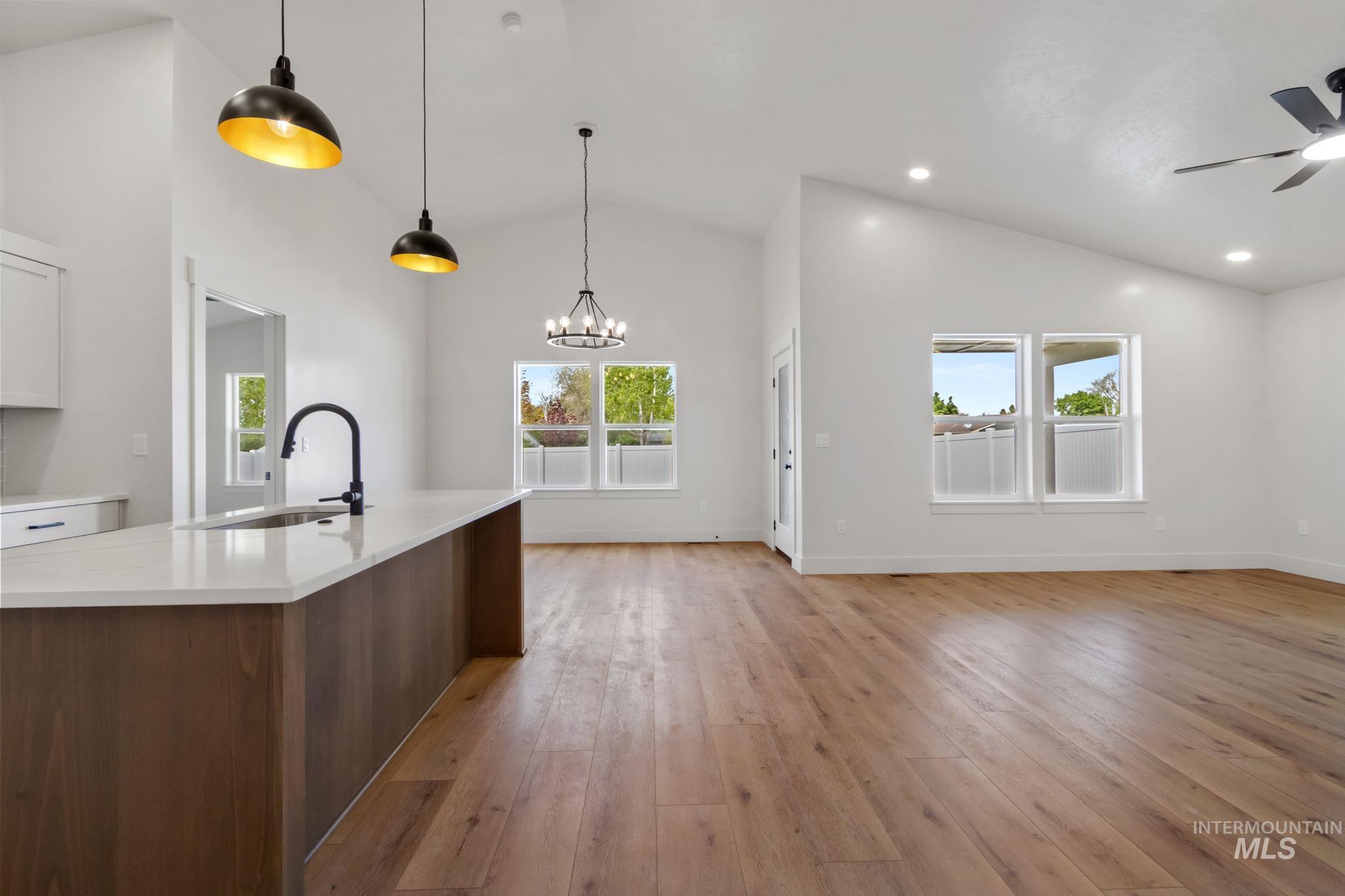321 North 11th Street Parma, ID 83660 - Photo 10 of 36 Open-concept living area featuring vaulted ceilings, wood-finish flooring, a kitchen island with a single basin sink and black faucet, recessed lighting, and multiple windows