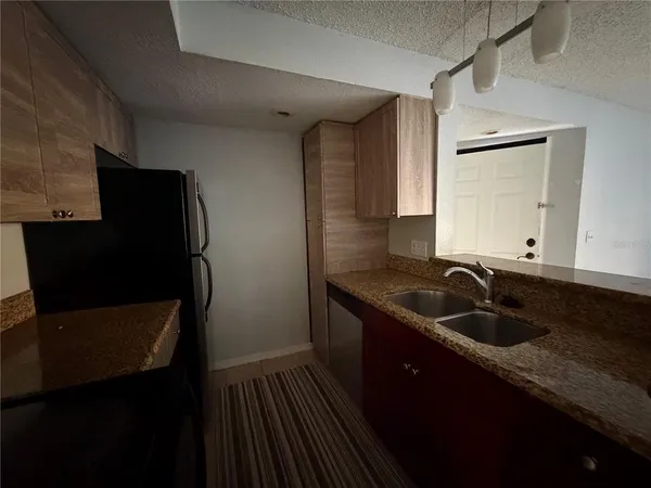a kitchen with granite countertop a refrigerator a sink and wooden cabinets