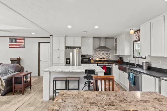 a kitchen with stainless steel appliances kitchen island granite countertop a table chairs sink and cabinets