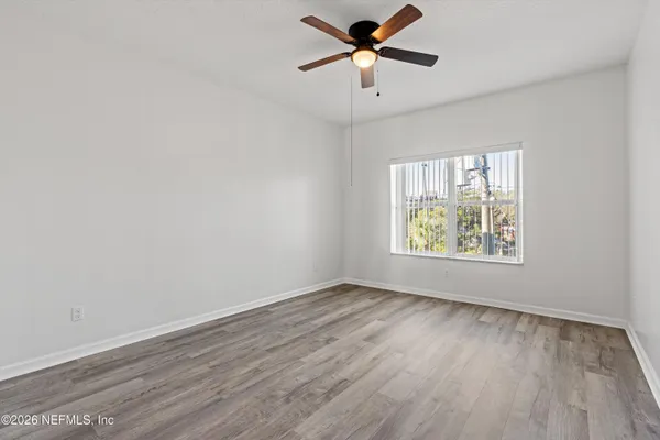 an empty room with wooden floor ceiling fan and windows