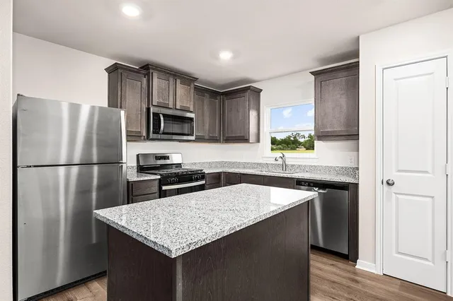 a kitchen with granite countertop a refrigerator a stove a sink a counter space and cabinets