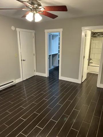 a view of an empty room with wooden floor and a fan