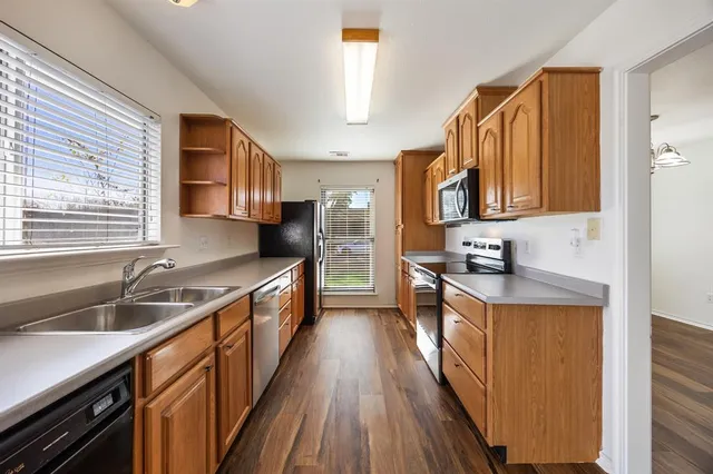 a kitchen with stainless steel appliances granite countertop wooden cabinets a sink dishwasher a stove and a refrigerator with wooden floor