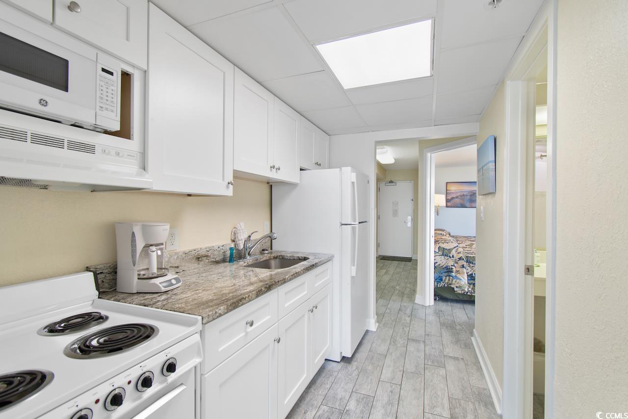 2300 North Ocean Boulevard, Unit 830 Myrtle Beach, SC 29577 - Photo 15 of 33 Kitchen with white appliances, white cabinetry, light wood-style flooring, a drop ceiling, and light stone counters