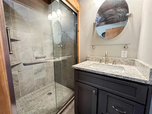 a bathroom with a granite countertop sink a mirror and shower