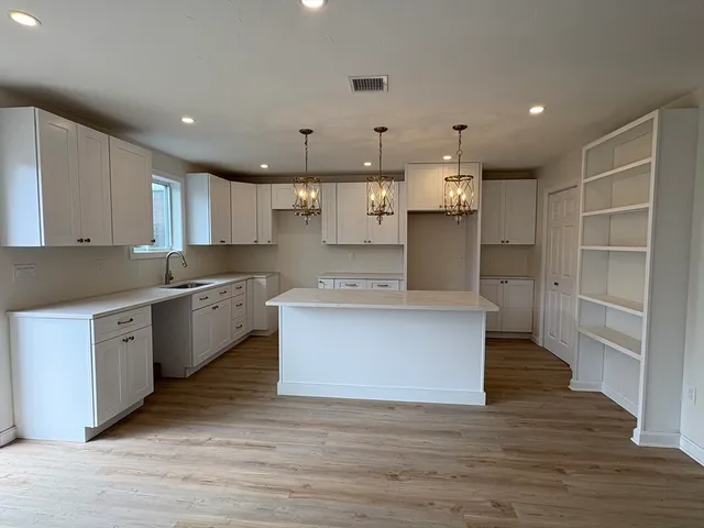 a large kitchen with stainless steel appliances granite countertop a large counter top a sink dishwasher a refrigerator and white cabinets with wooden floor