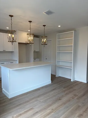 a room with kitchen island a chandelier and wooden floor