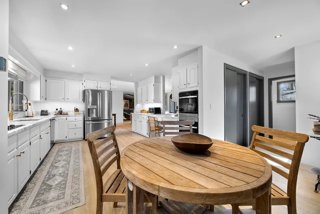 a kitchen with stainless steel appliances kitchen island granite countertop a dining table chairs refrigerator sink and cabinets