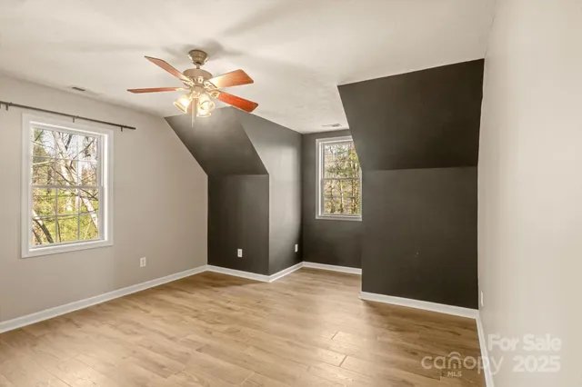 an empty room with wooden floor fan and windows