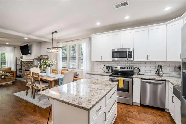 a kitchen with stainless steel appliances granite countertop a stove top oven a sink dishwasher a dining table and chairs with wooden floor