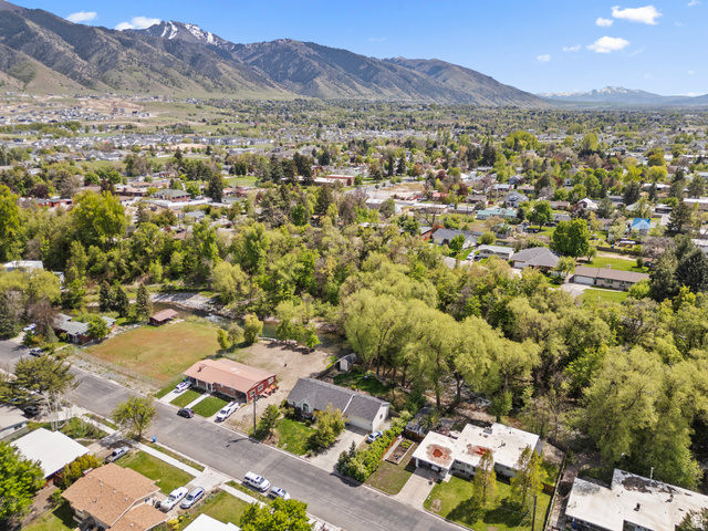 472 East 300 South Logan, UT 84321 - Photo 5 of 9 Expansive aerial showcasing a residential area with lush green trees, snow-capped mountains, and a clear blue sky