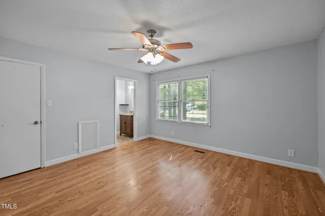 an empty room with wooden floor fan and windows