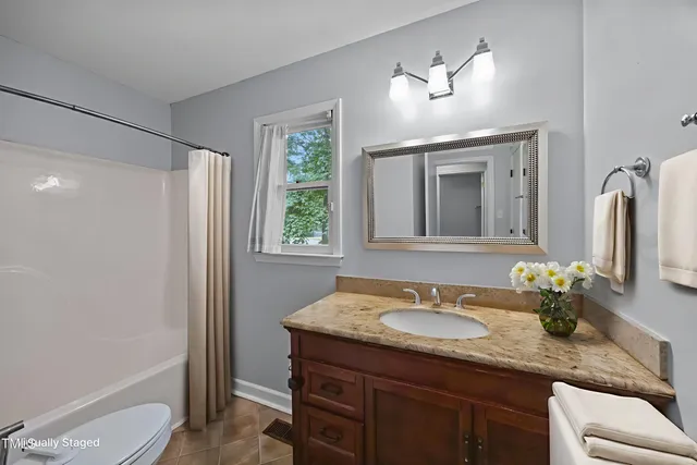 a bathroom with a granite countertop sink a toilet a mirror a vanity and shower
